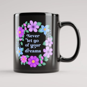 Black motivational mug with quote: Never let go of your dreams. Text with blue and violet floral wreath with green leaves and foliage.
