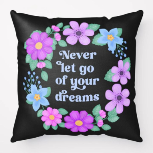 Motivational pillow with quote: Never let go of your dreams. Text with blue and violet floral wreath with green leaves and foliage on black background.