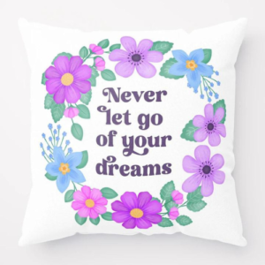 Motivational pillow with quote: Never let go of your dreams. Text with blue and violet floral wreath with green leaves and foliage on white background.