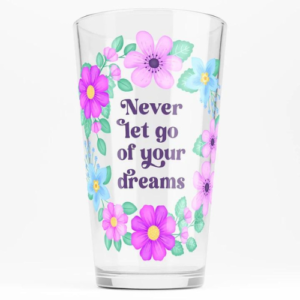 Motivational glass tumbler with quote: Never let go of your dreams. Text with blue and violet floral wreath with green foliage.